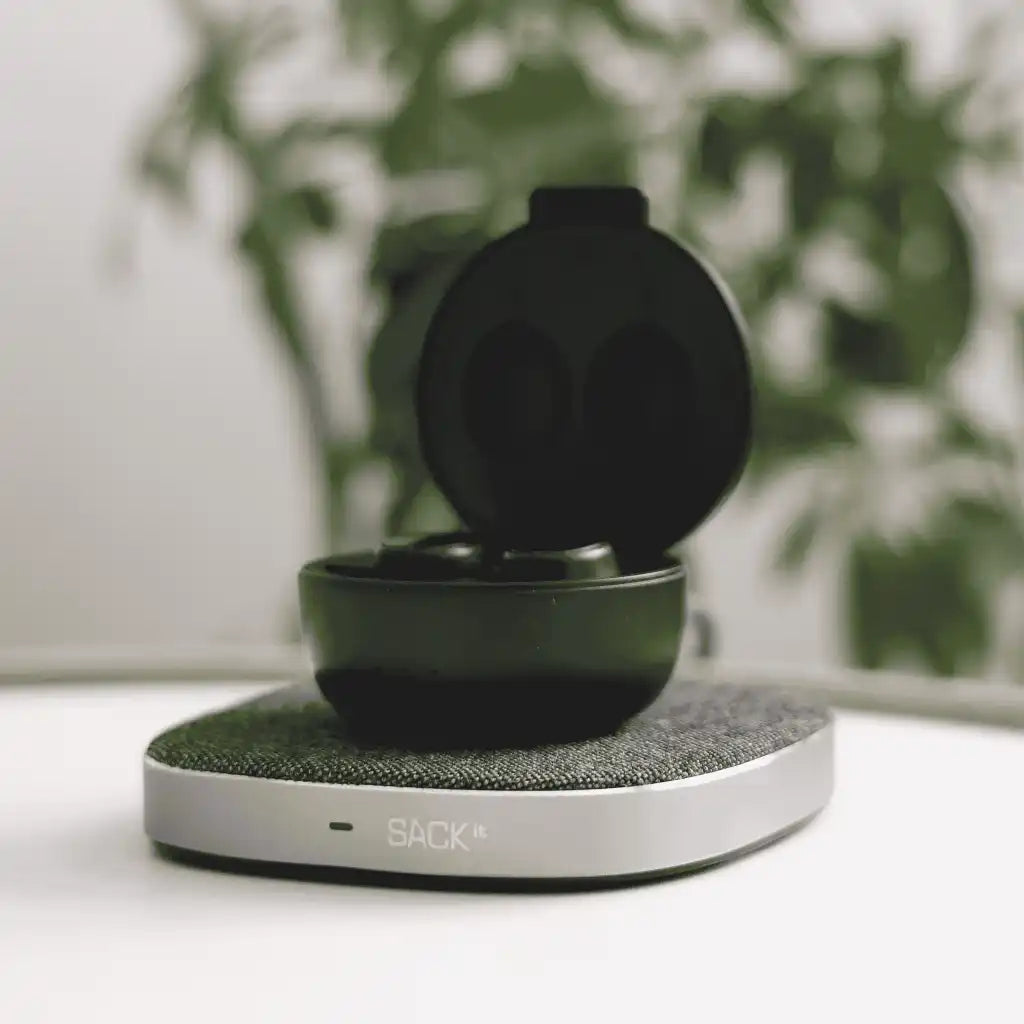 SACKit CHARGEit Dock Care -laturi pöydällä lataamassa SACKit-nappikuulokkeita – tyylikäs yrityslahja