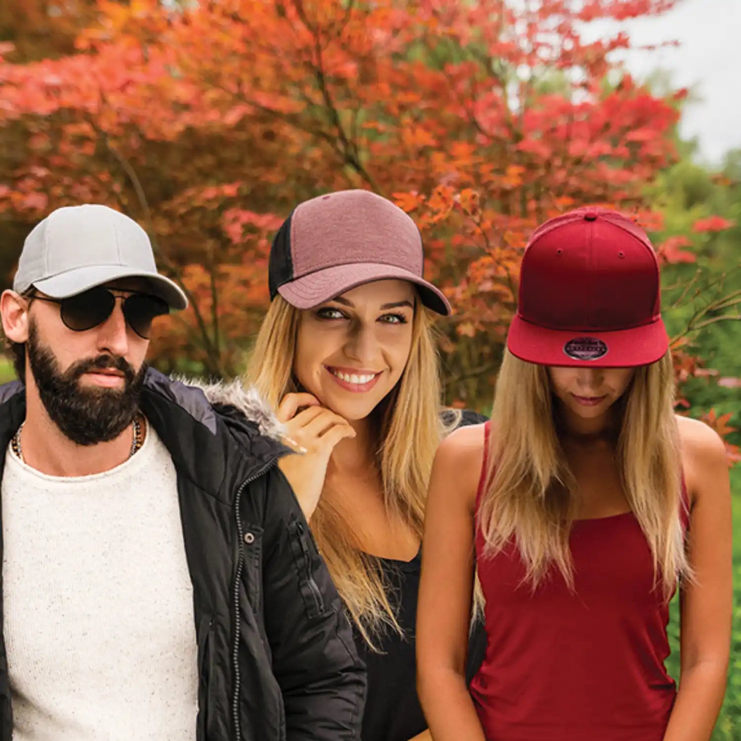 Kolme lippistÀ pukeneita ihmistÀ poseeraa yhdessÀ syksyisen lehvistön taustalla.