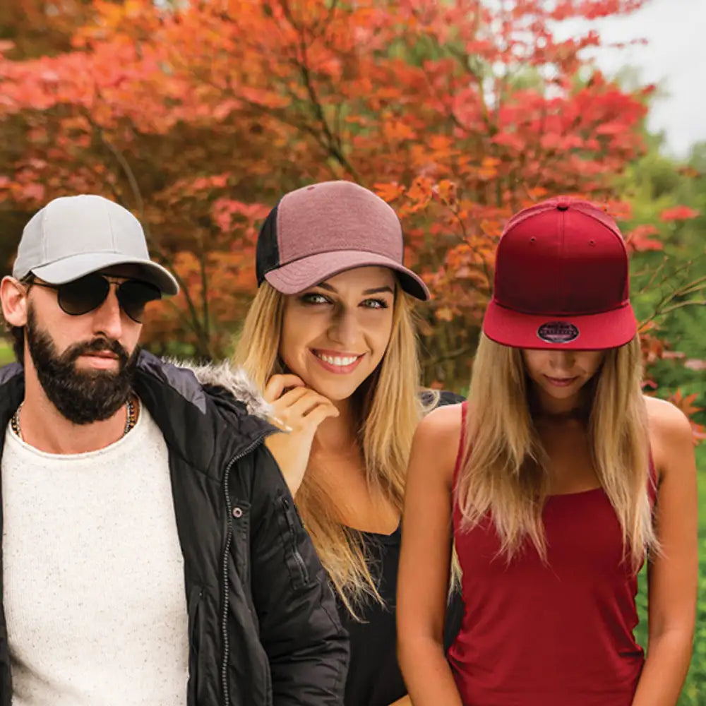 Kolme lippistä pukeneita ihmistä poseeraa yhdessä syksyisen lehvistön taustalla.