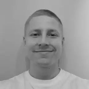 Mustavalkoinen lÀhikuva jostakin, joka pukeutuu valkoiseen t-paitaan ja hymyilee hieman.