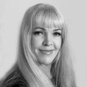 Musta-valkoinen muotokuva henkilöstÀ, jolla on pitkÀt vaaleat hiukset ja otsatukka, pukeutuneena tummiin vaatteisiin ja esittÀen lÀmmintÀ hymyÀ.