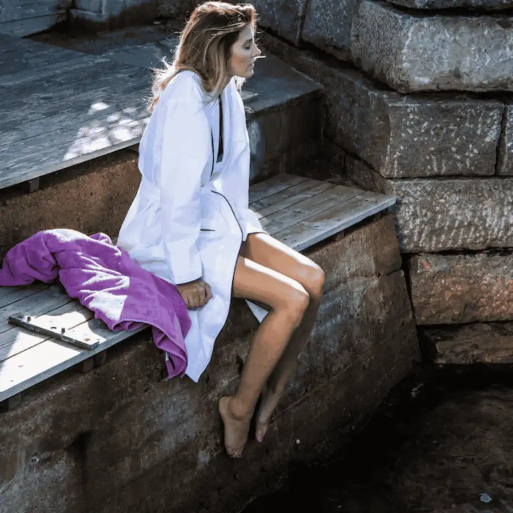 Nainen yllään valkoinen Queen Anne -kylpytakki rannalla – rentouttava liikelahjaidea