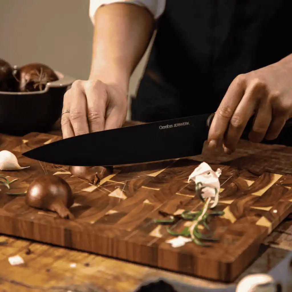 Akaasiapuinen Orrefors Jernverk -leikkuulauta käytössä sipulin pilkkomiseen